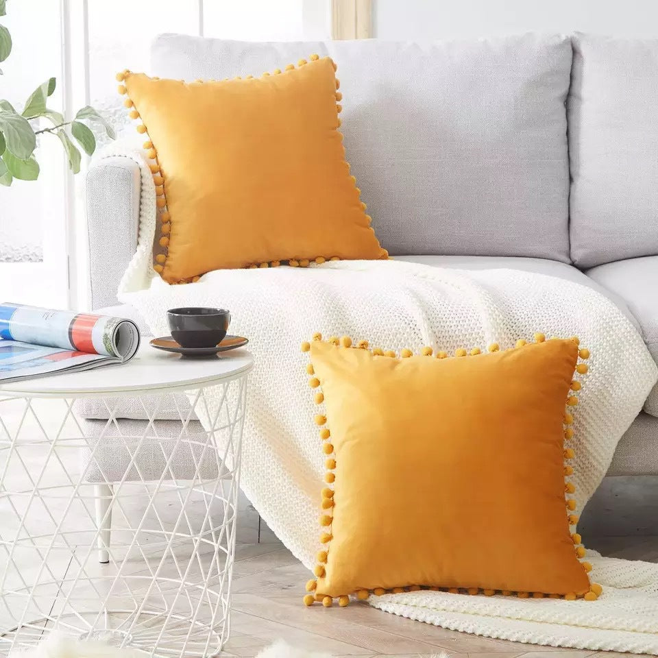 Housse de coussin en velours à pompons Nesty - Deux coussins jaune moutarde sur un canapé gris