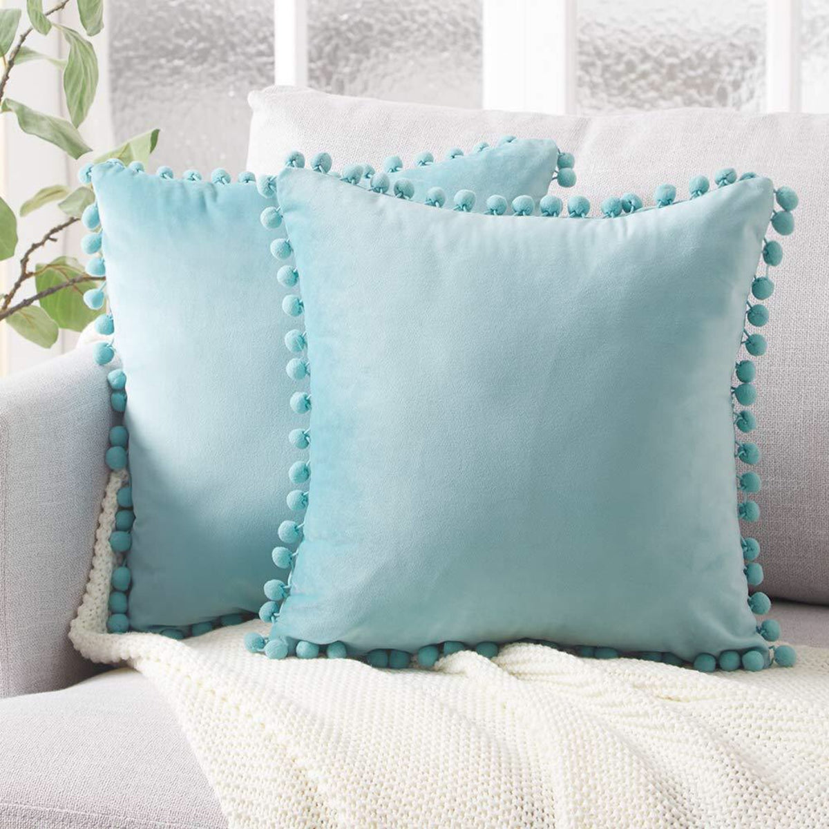 Housse de coussin en velours à pompons Nesty - Deux coussins bleu ciel sur un canapé clair