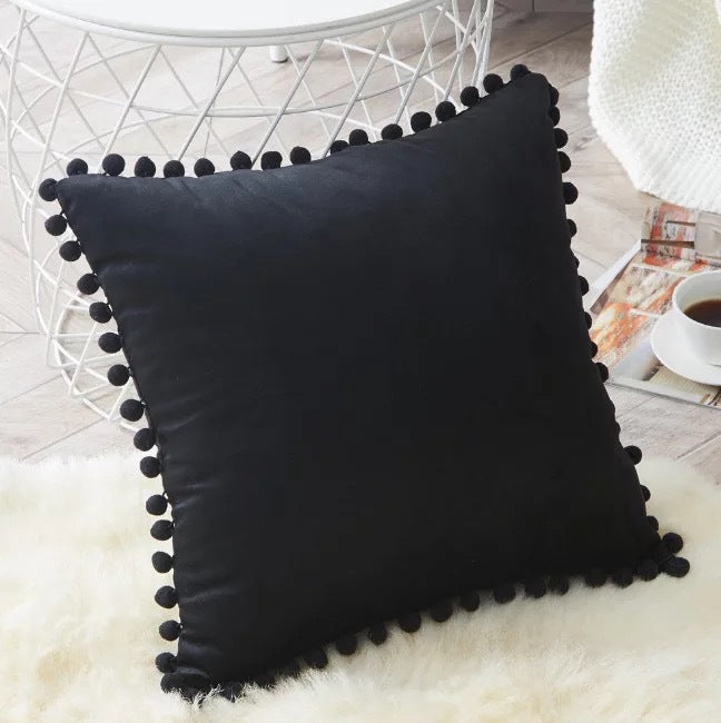 Housse de coussin en velours à pompons Nesty - Coussin noir posé sur un tapis en fausse fourrure blanche
