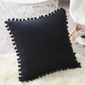 Housse de coussin en velours à pompons Nesty - Coussin noir posé sur un tapis en fausse fourrure blanche