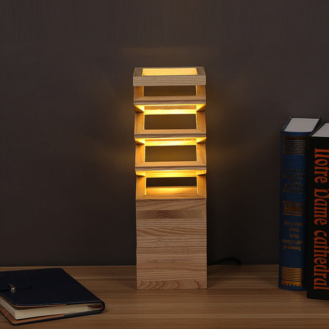 Lampe à poser créative en bois massif Nesty - Modèle à claire-voie empilée, posée sur un bureau avec livres