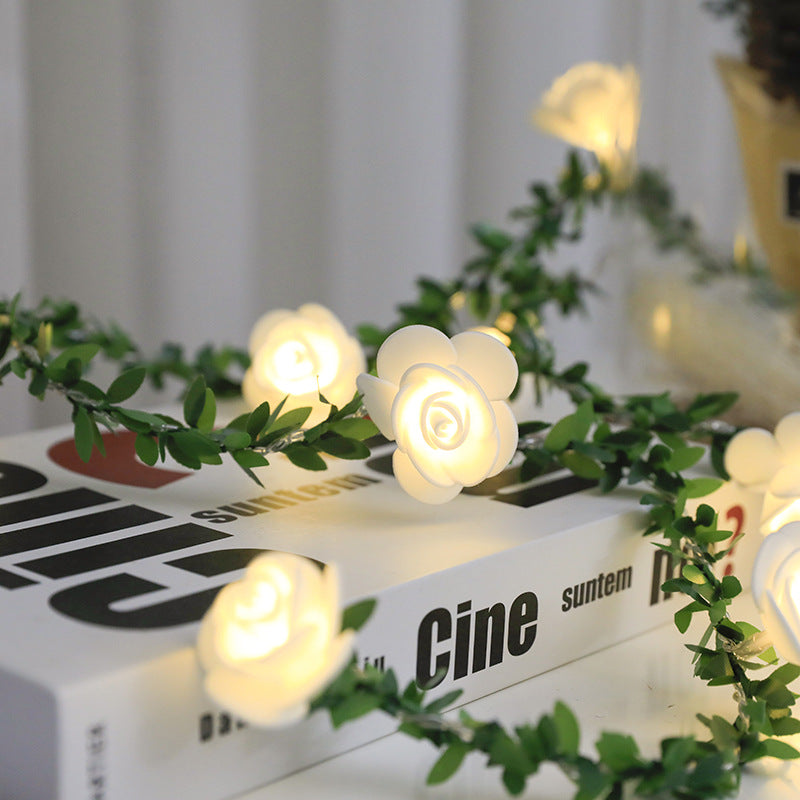 Guirlande lumineuse LED roses et lierre Nesty - Gros plan d'une rose lumineuse au milieu du feuillage sur une pile de livres