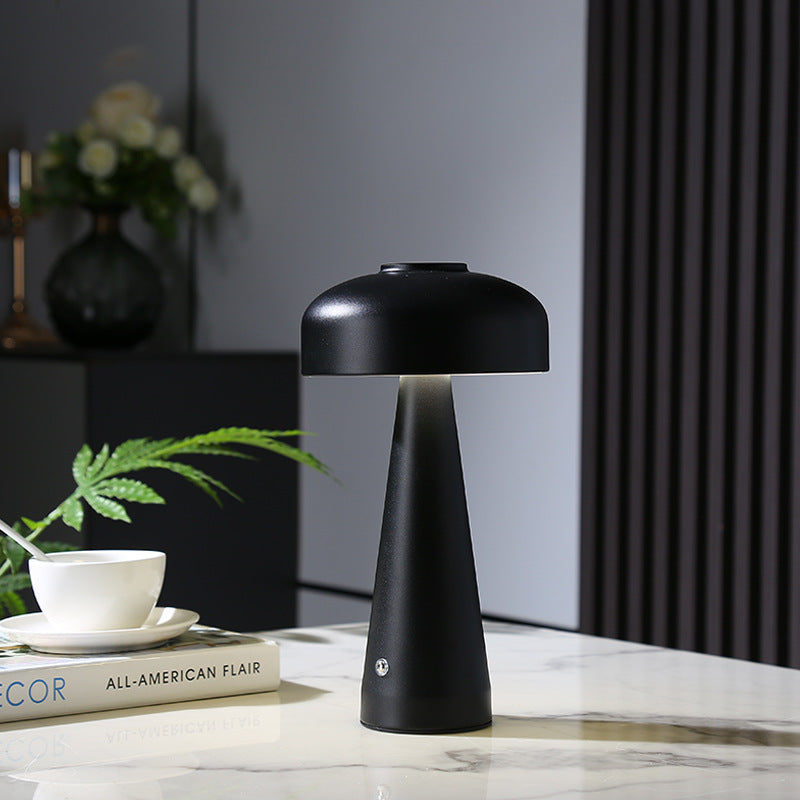 Lampe nomade champignon en céramique Nesty - Coloris noir, posée sur une table en marbre avec livres et plante