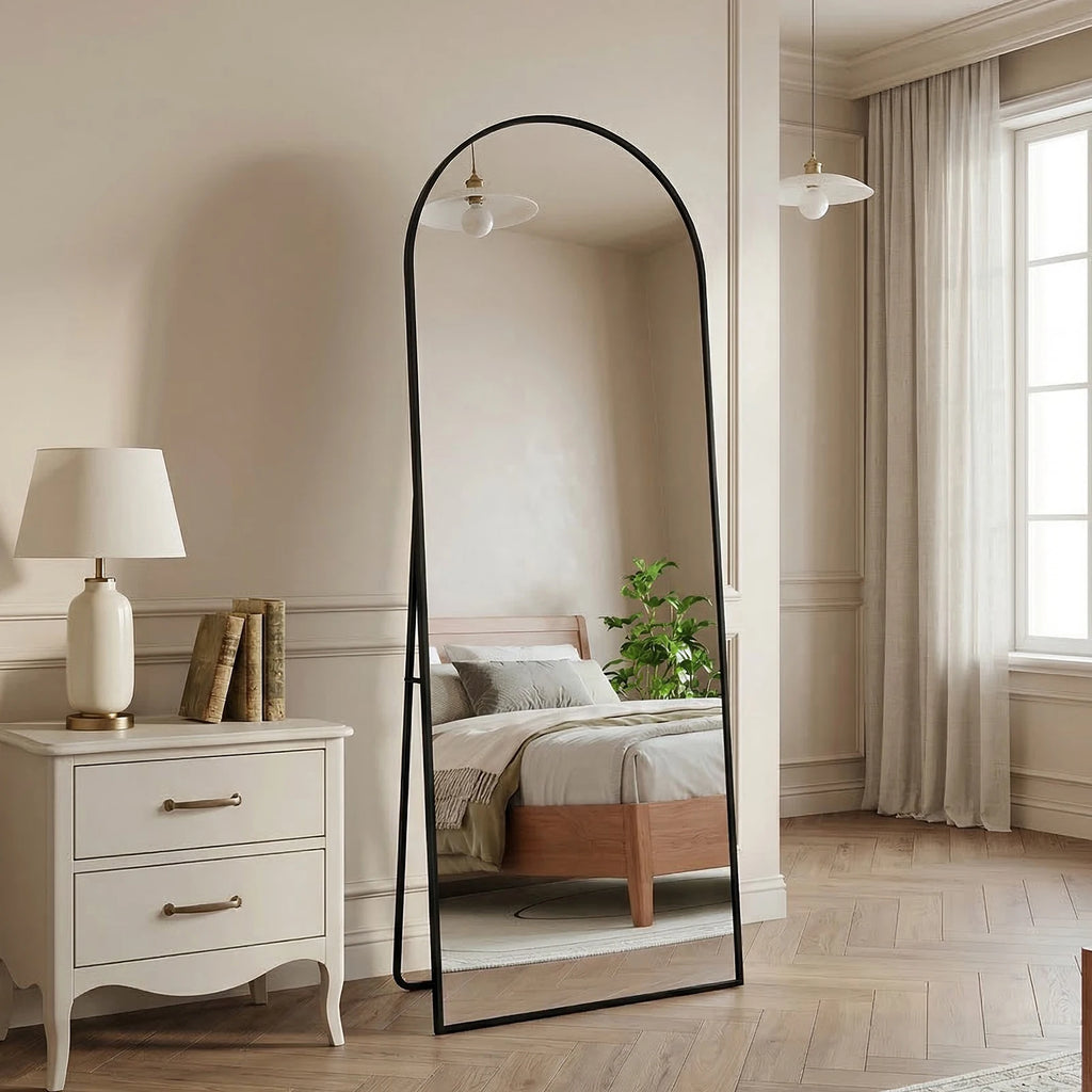 Miroir sur pied cintré noir Nesty - Support intégré, miroir cintré noir sur pied dans une chambre beige, près d'une table de chevet blanche avec lampe et livres