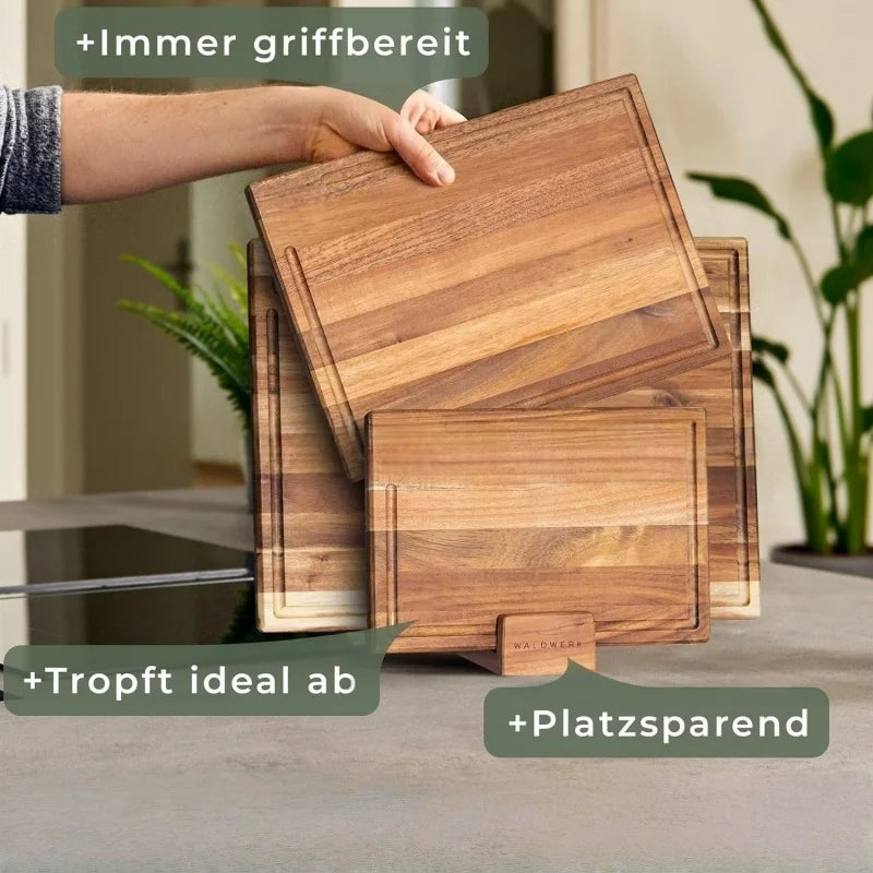 Set de 3 planches à découper en chêne avec rigole à jus Nesty, main soulevant une planche depuis le support en bois, texte en allemand (toujours à portée de main, s'égoutte, gain de place)