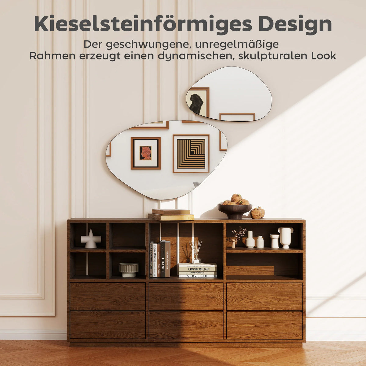 Duo de miroirs galets asymétriques, sur mur au-dessus d'un meuble bas avec livres et coupe de grenades, texte allemand 'Kieselsteinförmiges Design' - Nesty
