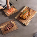Set de 3 planches à découper en chêne avec rigole à jus Nesty, trois planches avec saumon tranché, poulet rôti au romarin et steak tranché, sur plan de travail gris