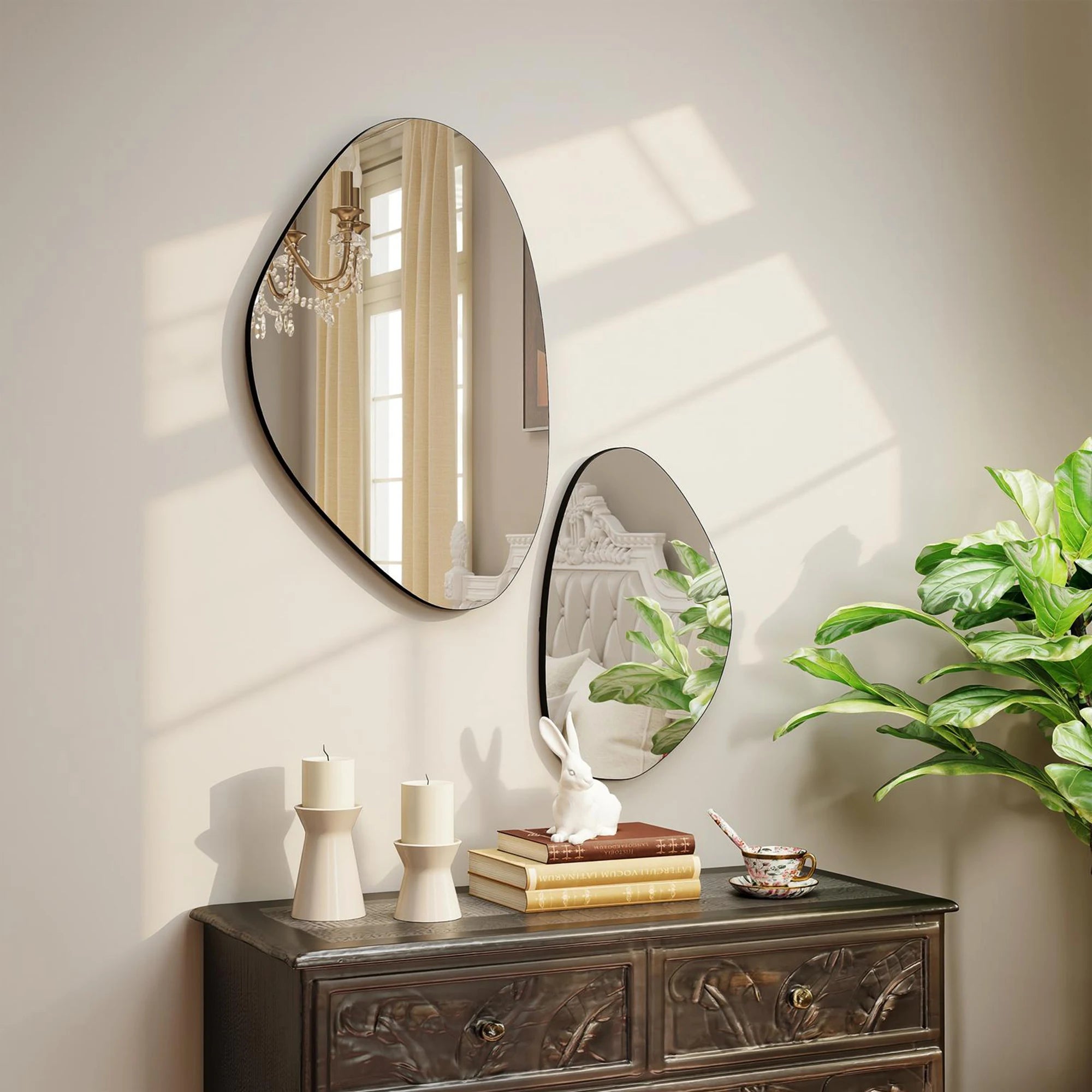 Duo de miroirs galets asymétriques à fin cadre noir, sur mur au-dessus d'une commode ancienne avec bougeoirs et figurine lapin - Nesty