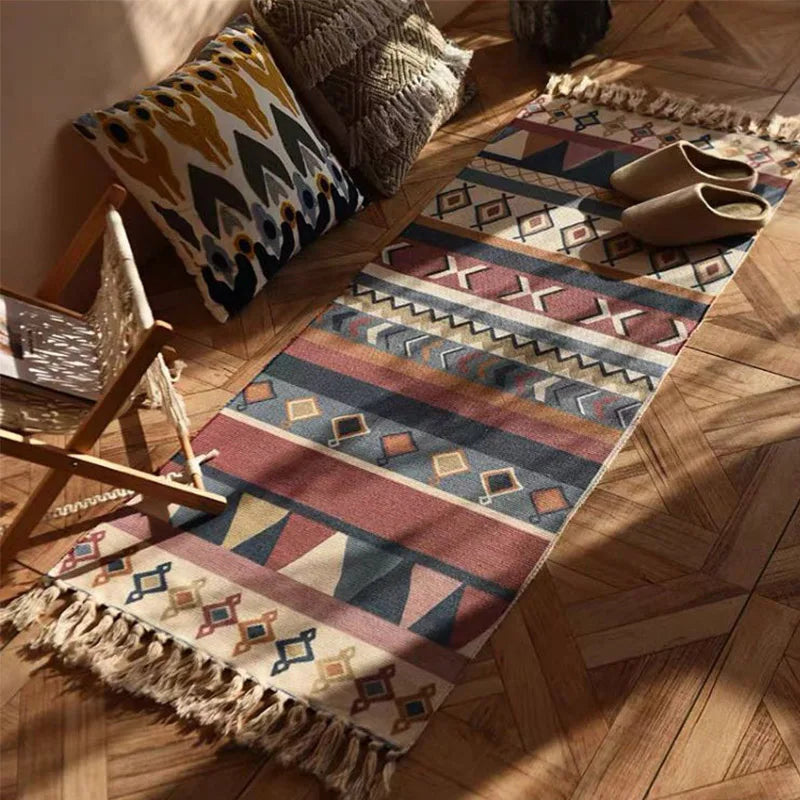 Tapis vintage à carreaux — coton, esprit bohème - Nesty, tapis chemin à motifs aztèques multicolores avec franges, posé près d'un fauteuil bohème avec coussins et chaussons