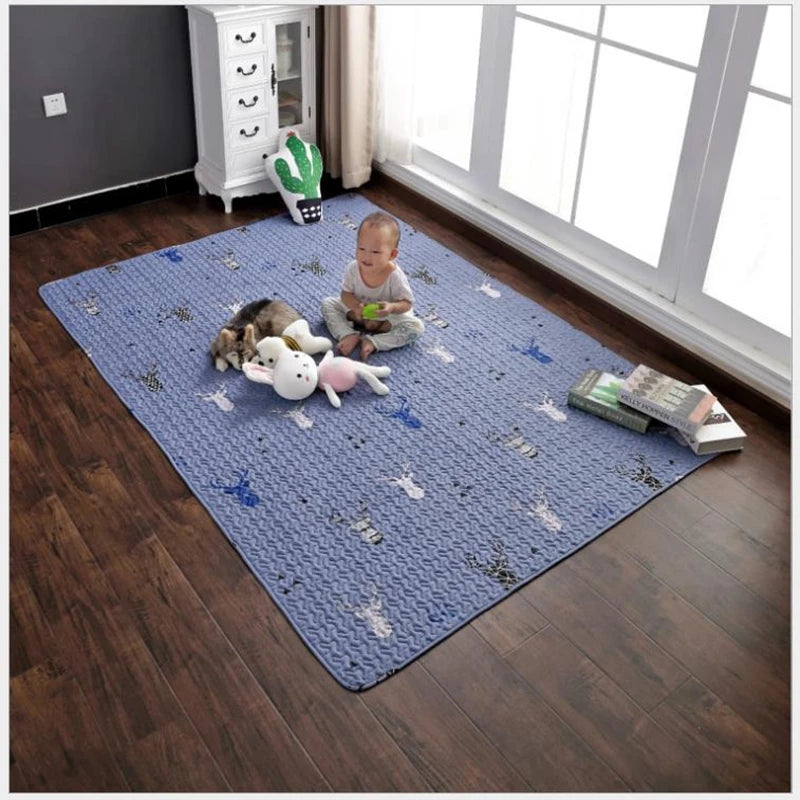 Tapis épais pour bébé — coin jeux - Nesty, variante bleue à motif cerfs, bébé assis avec des peluches dessus