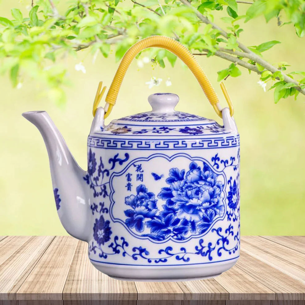 Théière en porcelaine bleu et blanc, grande capacité 2L Nesty, motif pivoines et idéogrammes chinois, anse en rotin tressé jaune, sur planche en bois devant un feuillage