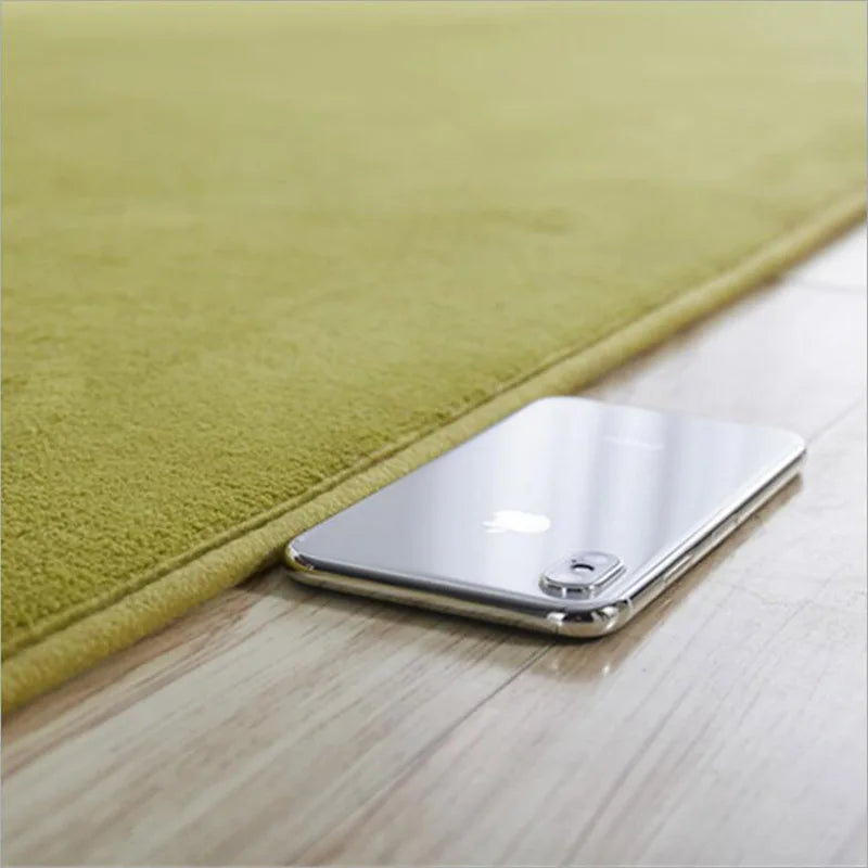 Gros plan sur le bord d'un tapis en velours vert olive posé sur un parquet, avec un smartphone à côté pour montrer l'épaisseur.