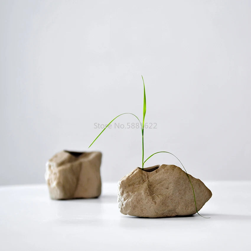 Vase en céramique et pierre, forme organique moderne Nesty, deux vases en forme de pierre brute, l'un garni d'un brin d'herbe verte, sur fond gris clair