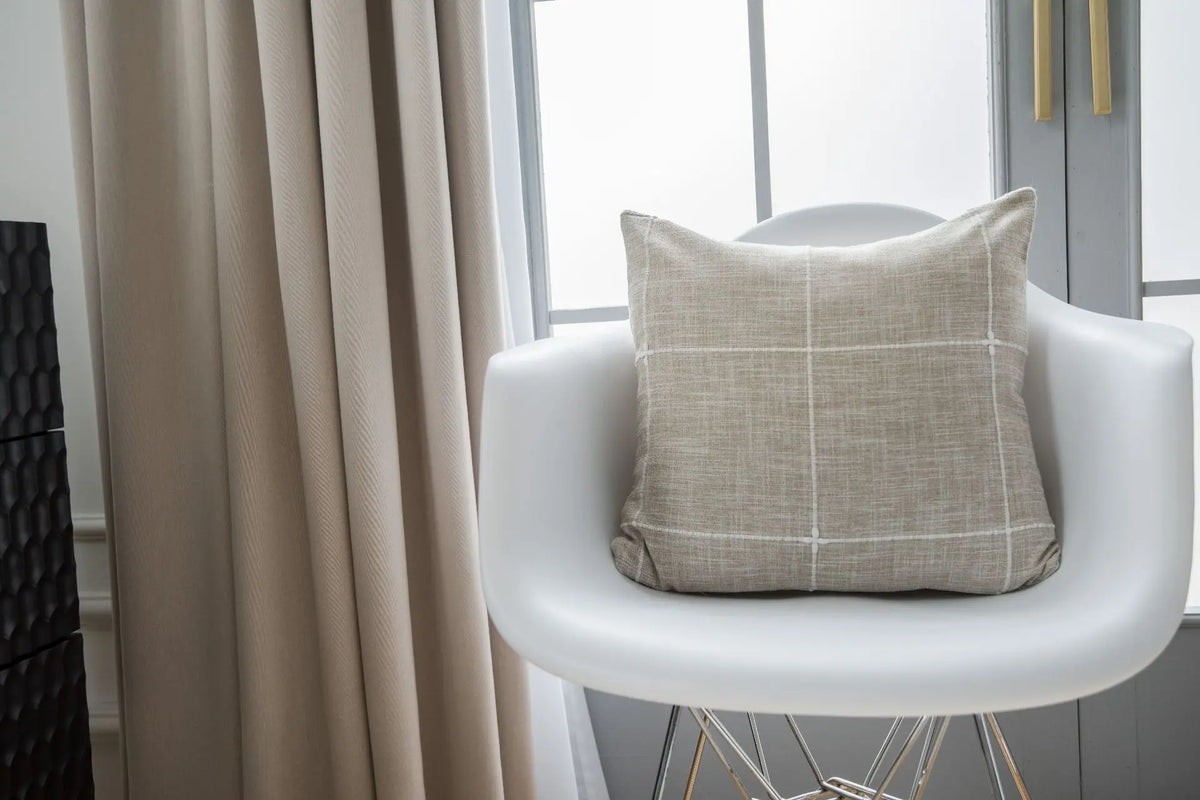 Housse de coussin en coton et lin, rouge écarlate, matière épaisse Nesty, housse de coussin à carreaux beige et blanc posée sur fauteuil design blanc devant une fenêtre