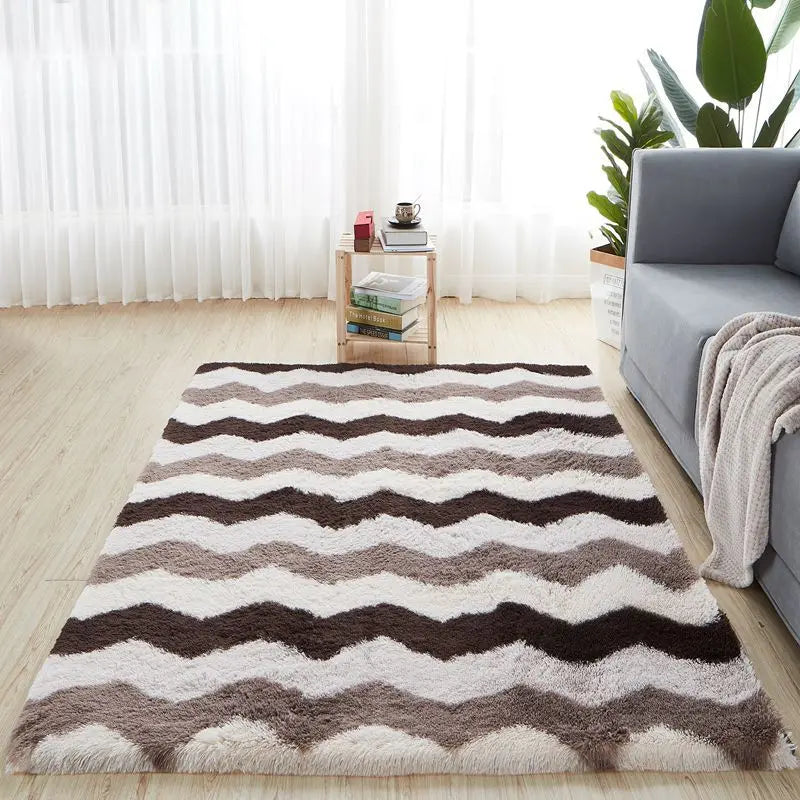 Tapis à motif chevron marron, beige et blanc, posé au sol dans un salon devant un canapé gris et une desserte en bois.