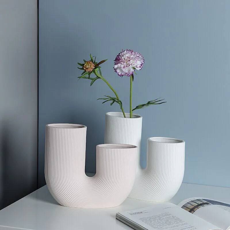 Vase céramique forme U, style nordique épuré - Nesty - Trois tailles en forme de U, coloris rose pâle et blanc, l'un garni d'une fleur mauve, sur une table près d'un livre