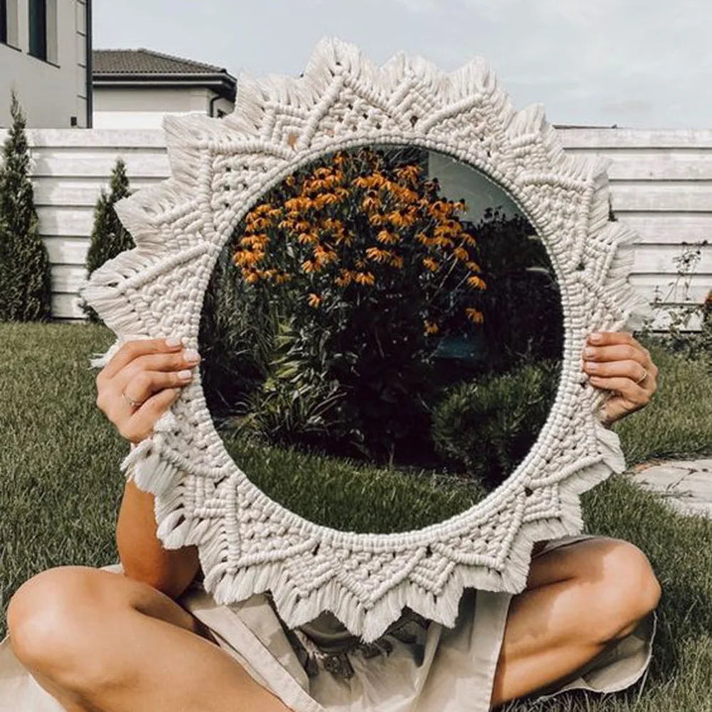 Miroir mural macramé rond à cadre tressé étoilé, tenu devant le visage par une personne assise dans un jardin fleuri - Nesty