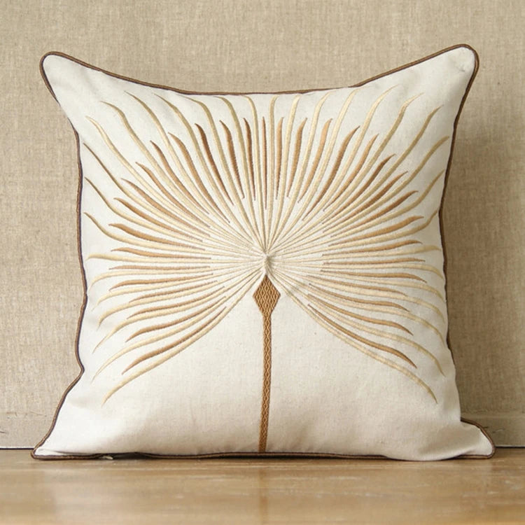 Housse de coussin en coton et lin, broderie pissenlit Nesty, housse de coussin écrue brodée d'une feuille de palmier stylisée dorée et beige, bordure marron, posée contre un mur en lin