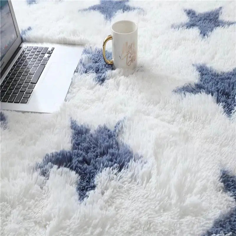 Gros plan sur un tapis blanc à motifs d'étoiles bleu marine, avec un ordinateur portable et une tasse posés dessus.