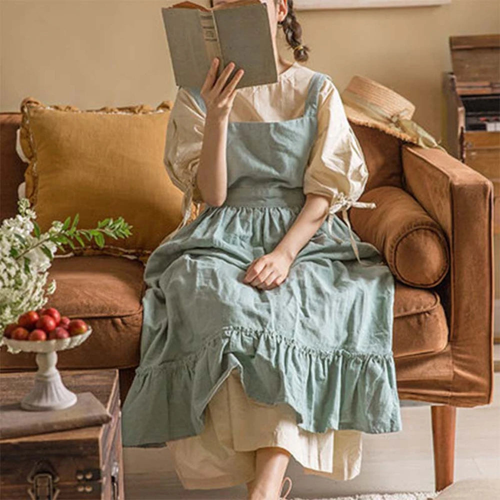 Femme assise sur un canapé lisant un livre, tablier en coton et lin vert sauge à volant, style pastoral français - Nesty