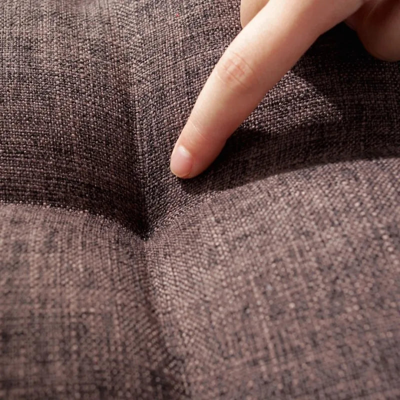 Grand coussin de sol carré en coton et lin, esprit tatami épais Nesty, gros plan sur le capitonnage matelassé brun d'un coussin, doigt posé sur la couture centrale