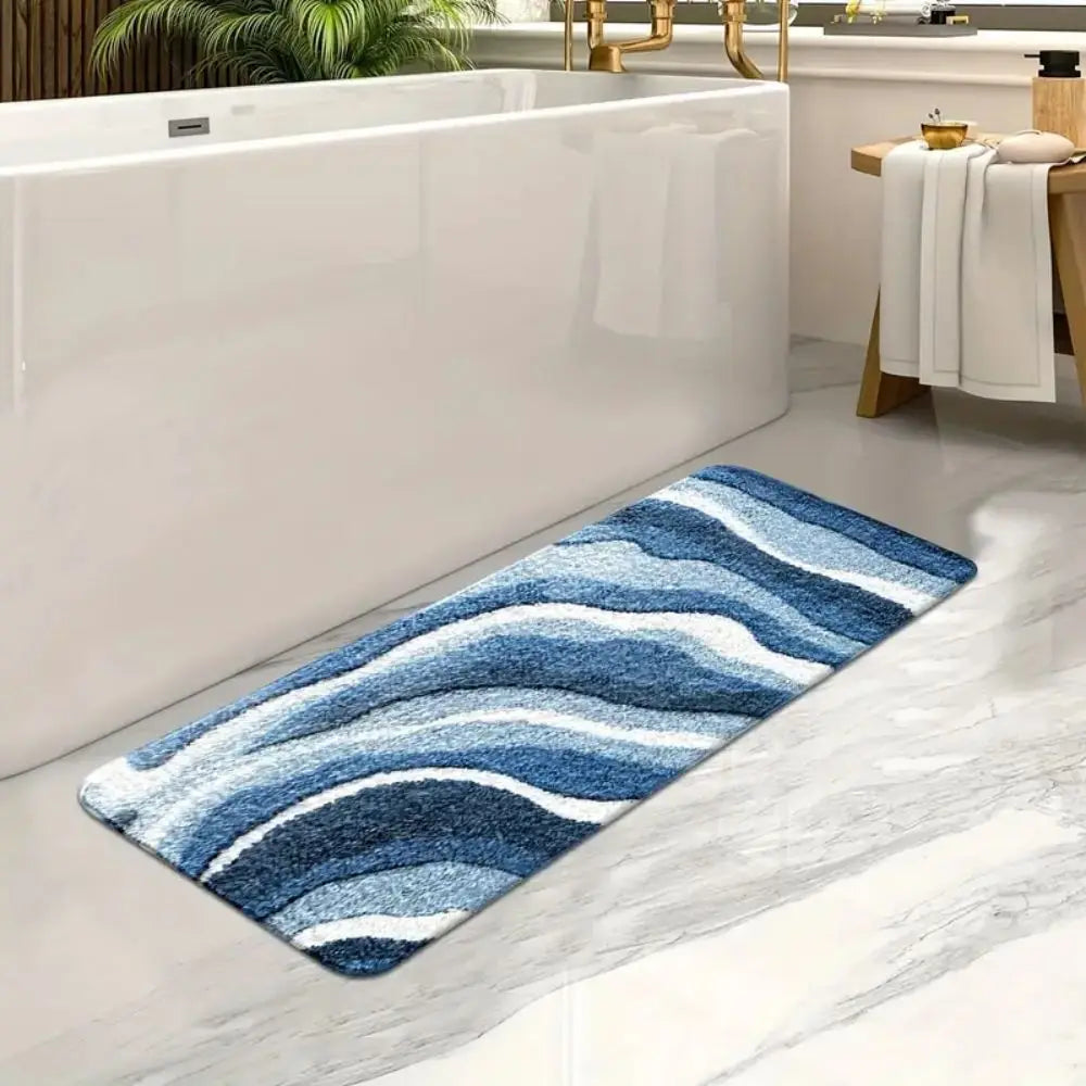 Tapis de bain à motif de vagues bleues, posé au sol devant une baignoire blanche.