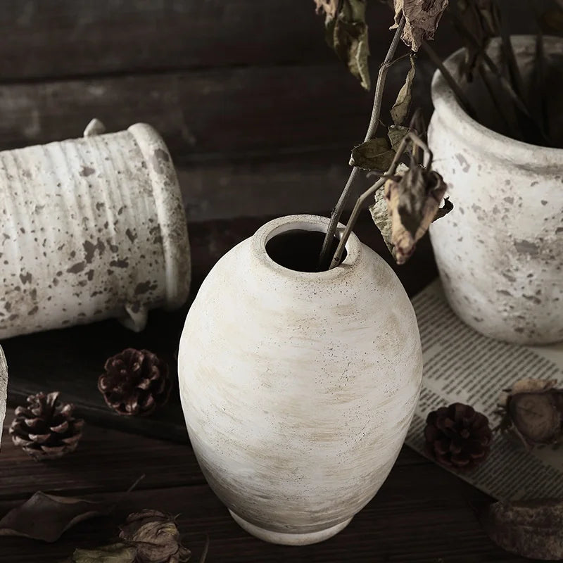 Vase céramique artisanal, style rétro fait main - Nesty - Vase ovoïde blanc patiné à effet vieilli, garni de feuillage séché, entouré de pots en céramique texturée et de pommes de pin