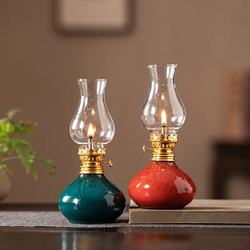 Lampe à huile en céramique Nesty - Deux lampes à huile céramique, verte et rouge, avec globe en verre et flamme allumée, sur une table