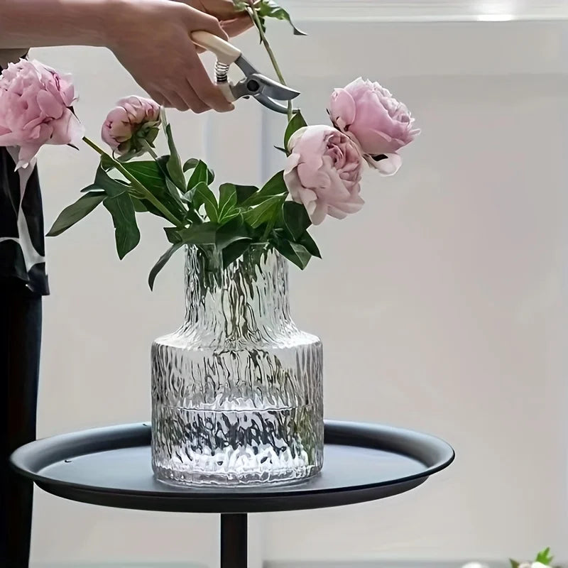Vase en verre soufflé texturé glacier, 8 cm de diamètre Nesty, main coupant une tige de pivoine rose au-dessus du vase, posé sur un plateau noir