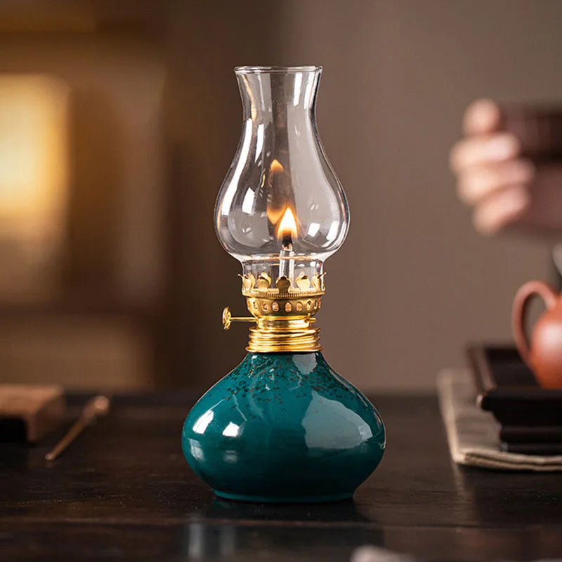 Lampe à huile en céramique Nesty - Lampe verte allumée sur une table sombre, main floutée tenant une théière en arrière-plan
