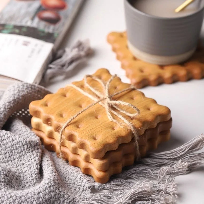 Pile de dessous de verre en bois forme biscuit ficelée, sur un plaid en tricot gris, avec tasse et magazine - Nesty