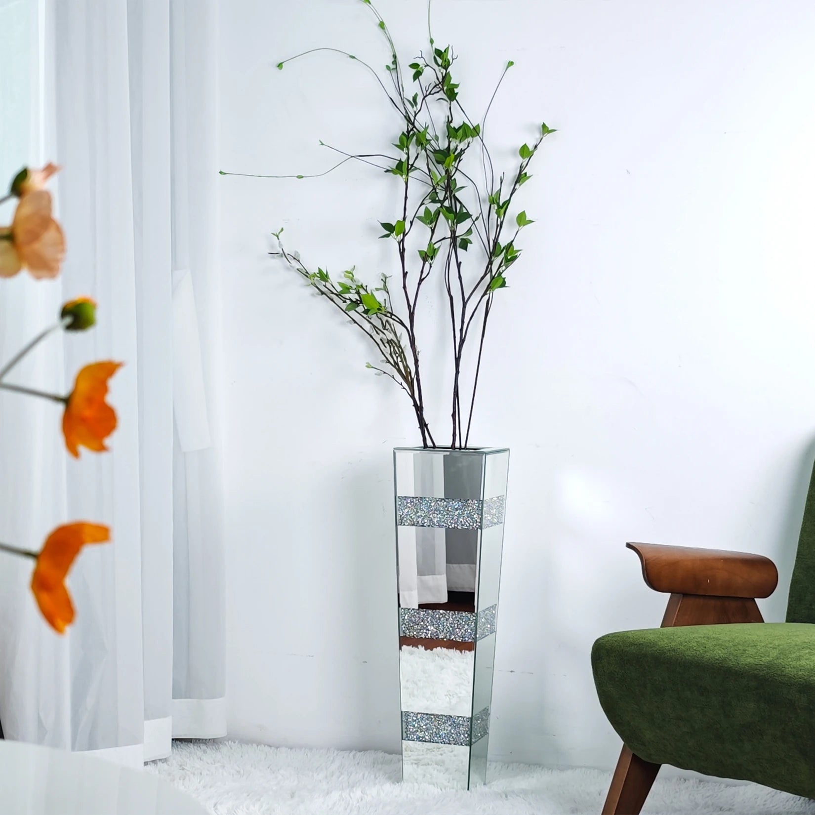 Vase sol en verre facetté, finition miroir - Nesty - Grand vase haut à bandes strassées et finition miroir argentée, garni de branches feuillues, dans un angle de salon près d'un fauteuil vert