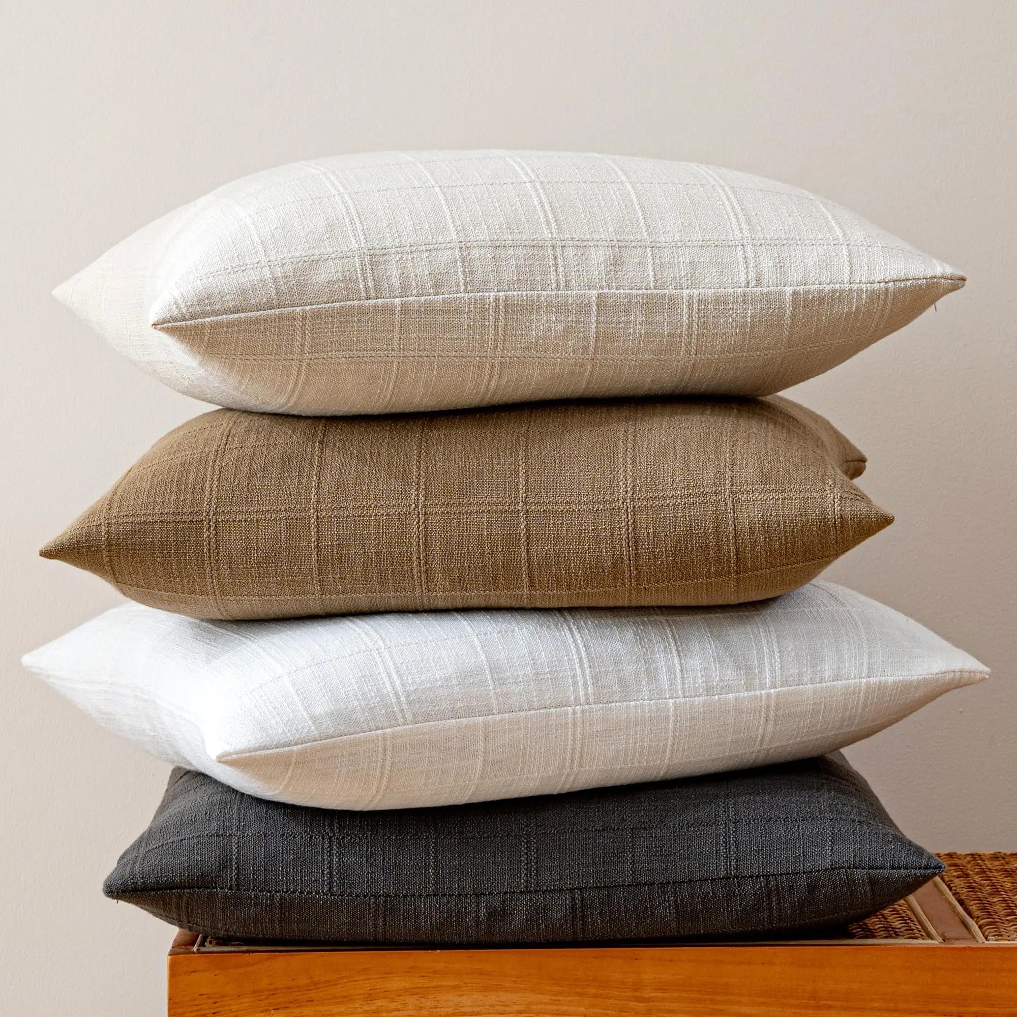 Housse de coussin en lin à carreaux, esprit campagne Nesty, quatre housses en lin à carreaux empilées de profil, coloris écru, camel, blanc et anthracite, montrant le tissage à carreaux