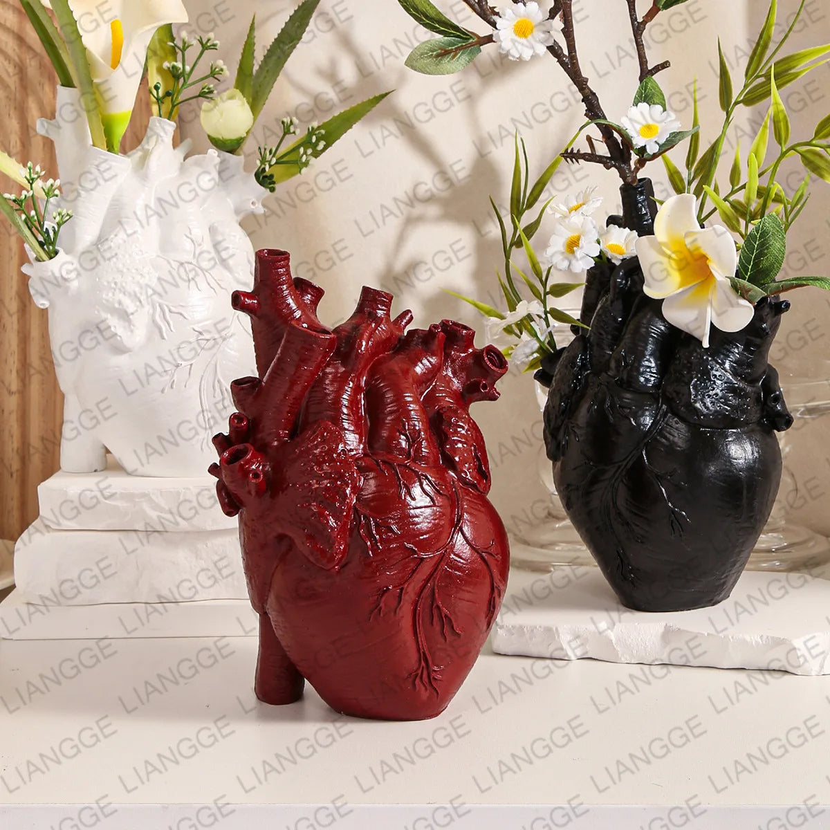 Vase en résine forme cœur, style nordique - Nesty - Trois coloris (blanc, rouge bordeaux, noir) en forme de cœur anatomique, garnis de fleurs blanches et de feuillage sur une table beige