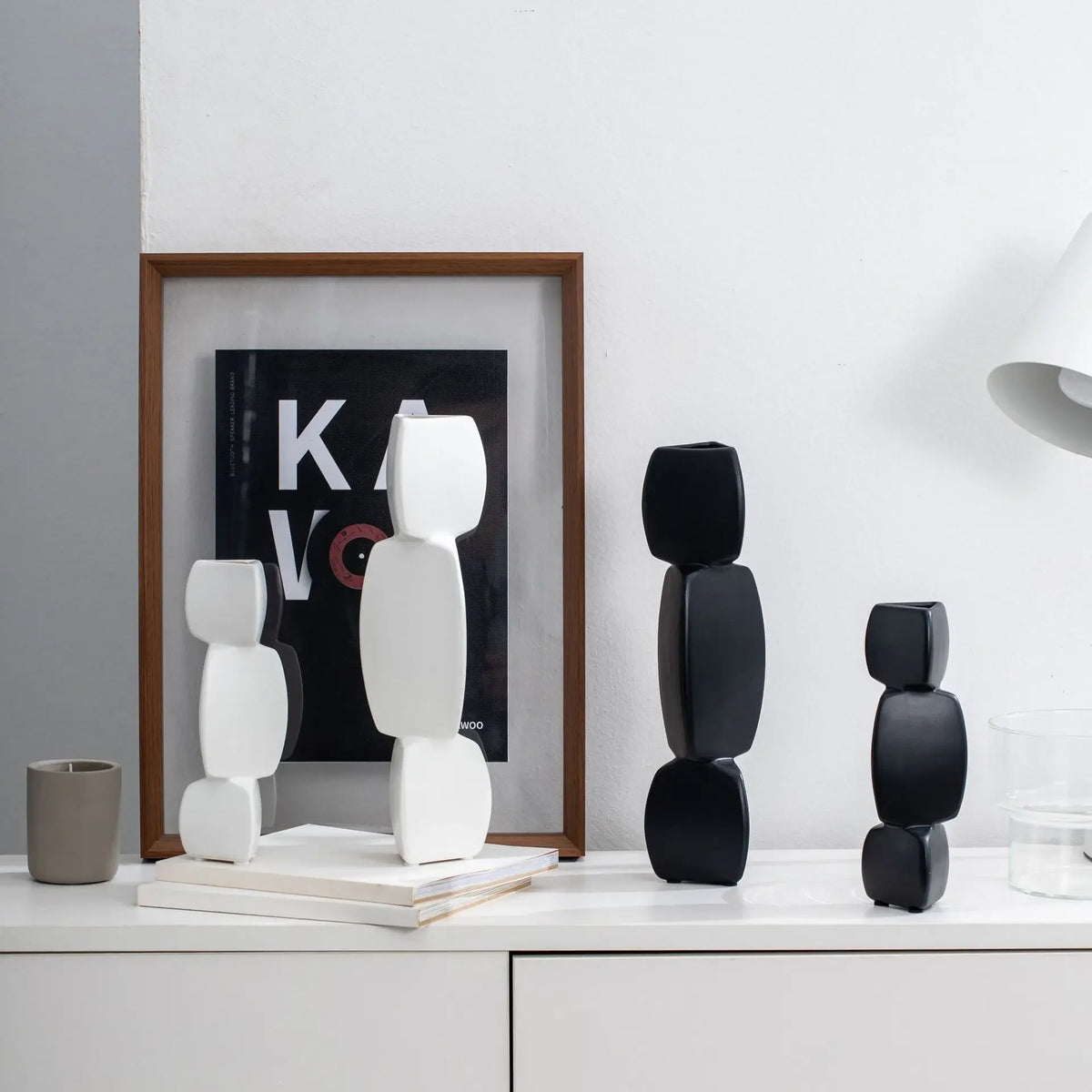 Vase noir en céramique Nesty - Modèles blancs et noirs empilés en galets, sur étagère avec affiche encadrée et livres