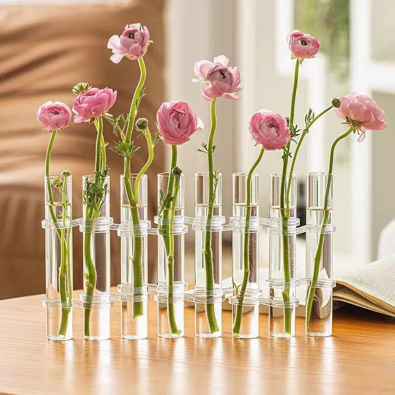Vase suspendu en verre pour bouturage, lot de tubes transparents Nesty, tubes articulés garnis de renoncules roses, sur table en bois avec livre ouvert