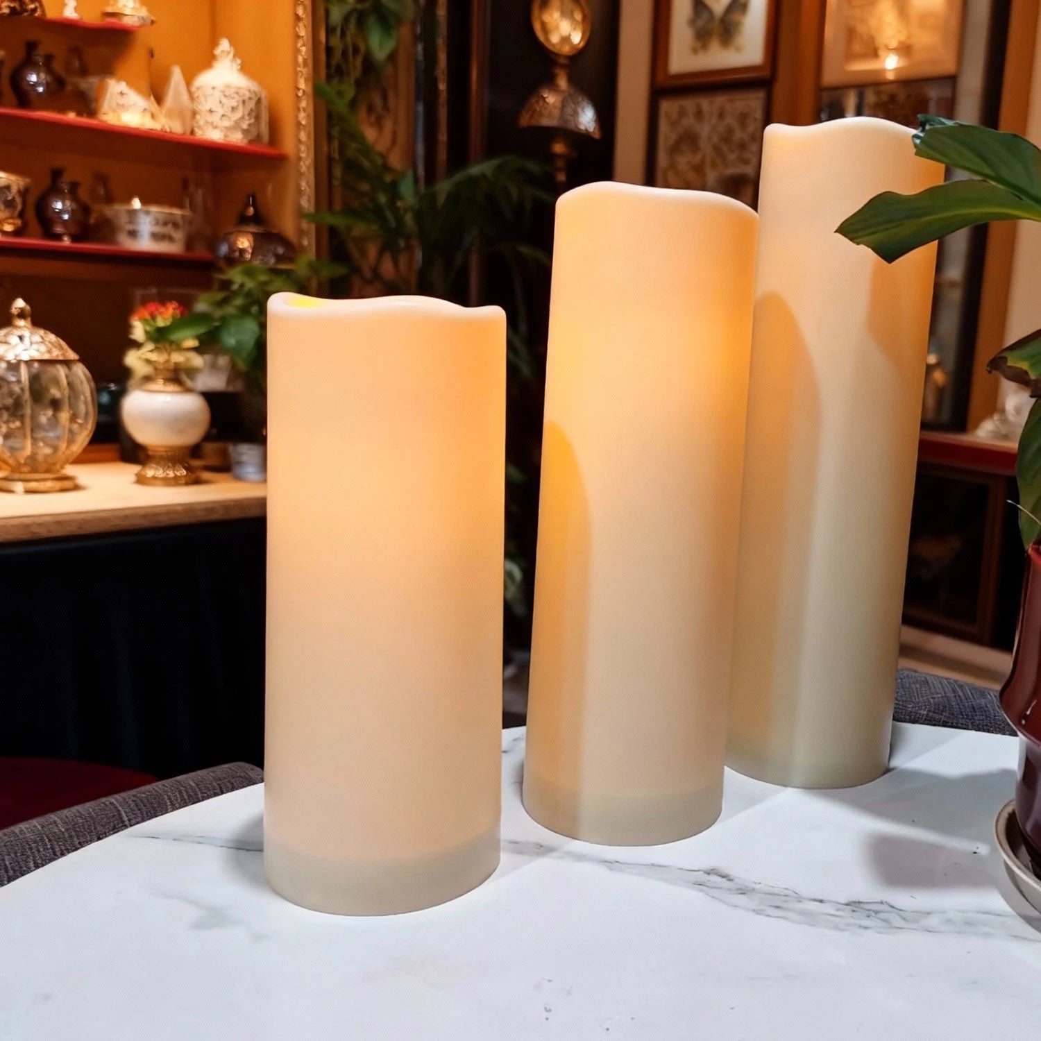 Bougies LED pilier vacillantes, télécommande, intérieur et extérieur Nesty, trois bougies LED pilier dans un intérieur oriental avec étagères d'objets décoratifs et plantes vertes
