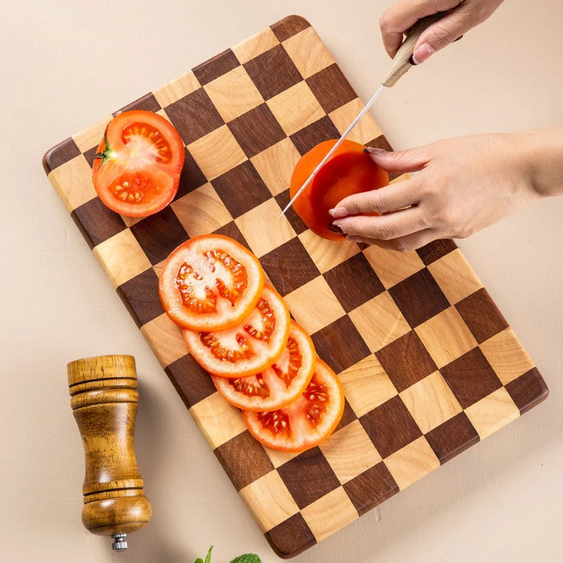 Planche à découper en bois massif, motif mosaïque Nesty, vue de dessus d'une main découpant des tranches de tomate au couteau sur la planche à damier