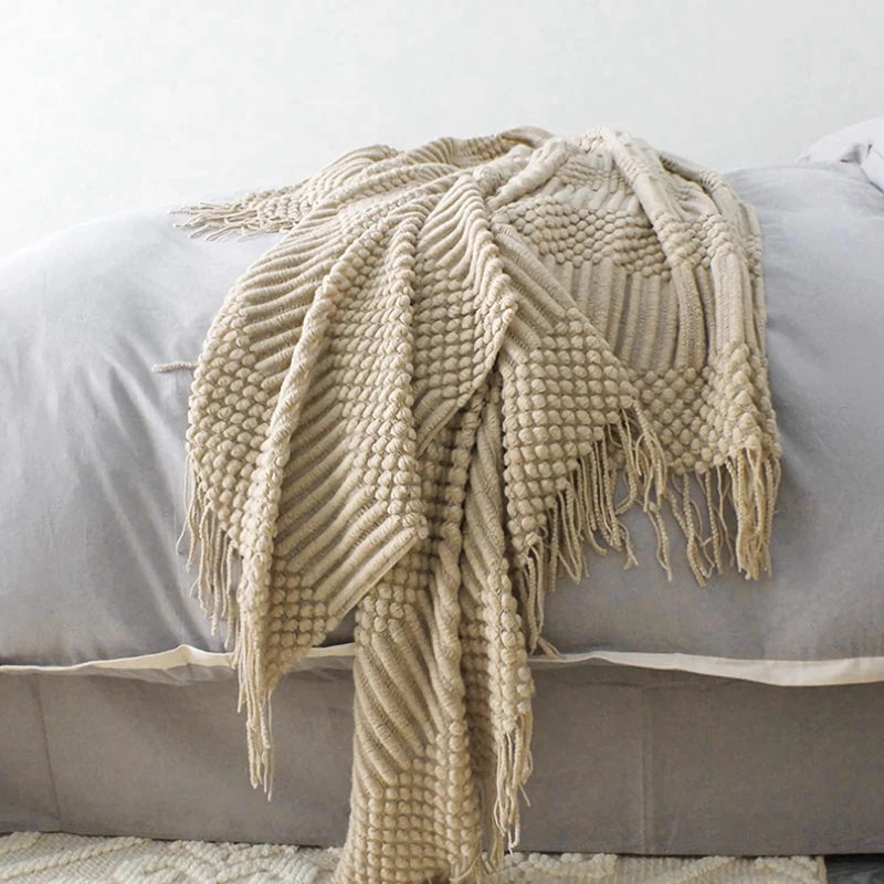 Plaid tricoté bohème kaki Nesty - Drapé sur lit avec oreillers gris, texture tissée et franges