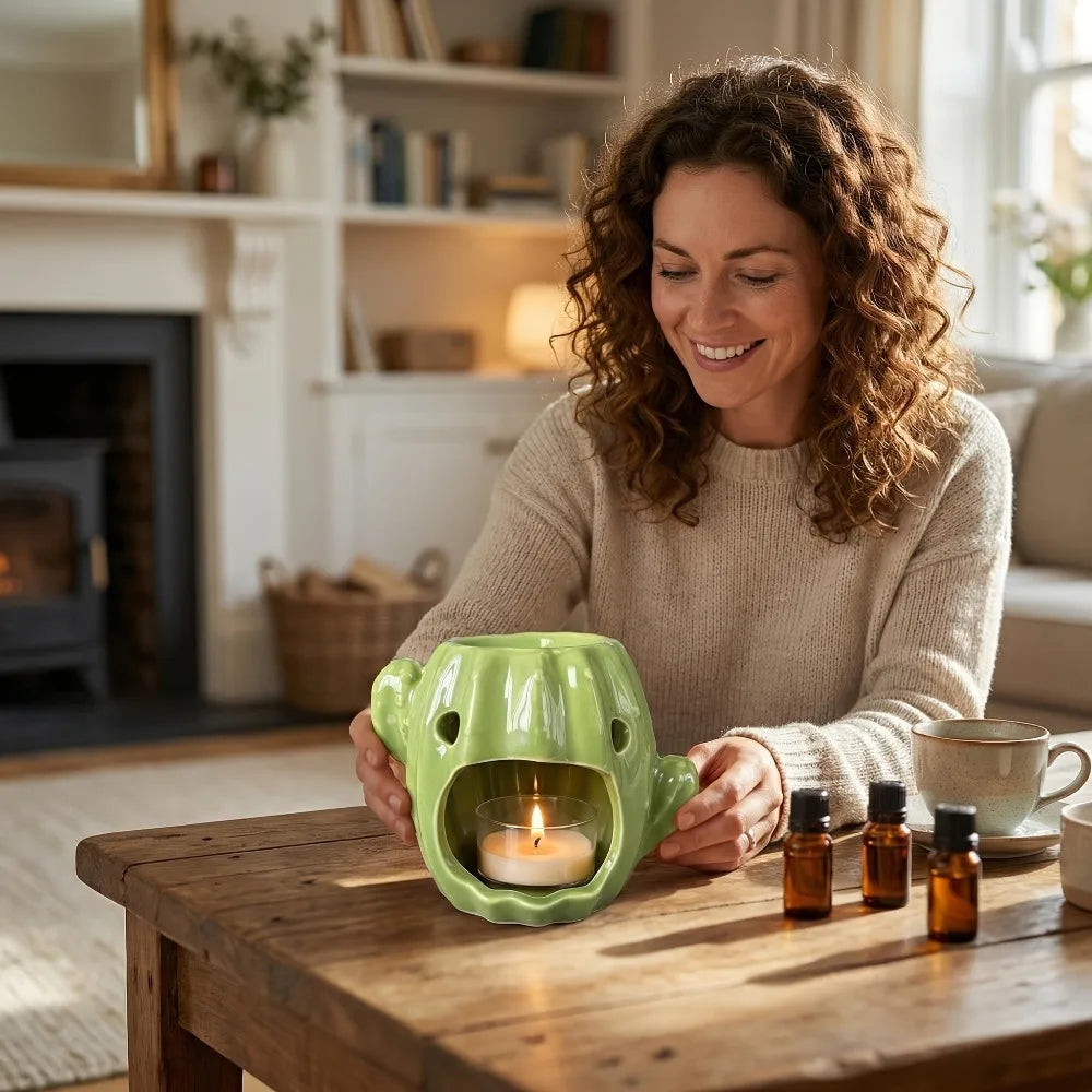 Diffuseur céramique cactus Nesty - Femme utilisant le brûle-huile vert en forme de cactus dans un salon, bougie allumée et flacons d'huiles essentielles à côté