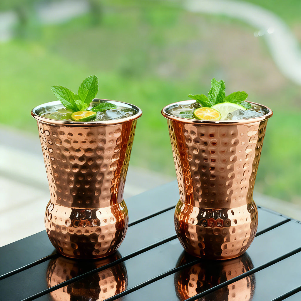 Gobelet tiki en inox cuivré, 350ml Nesty, deux gobelets martelés cuivrés garnis de glaçons, menthe et rondelles de citron vert, sur table extérieure