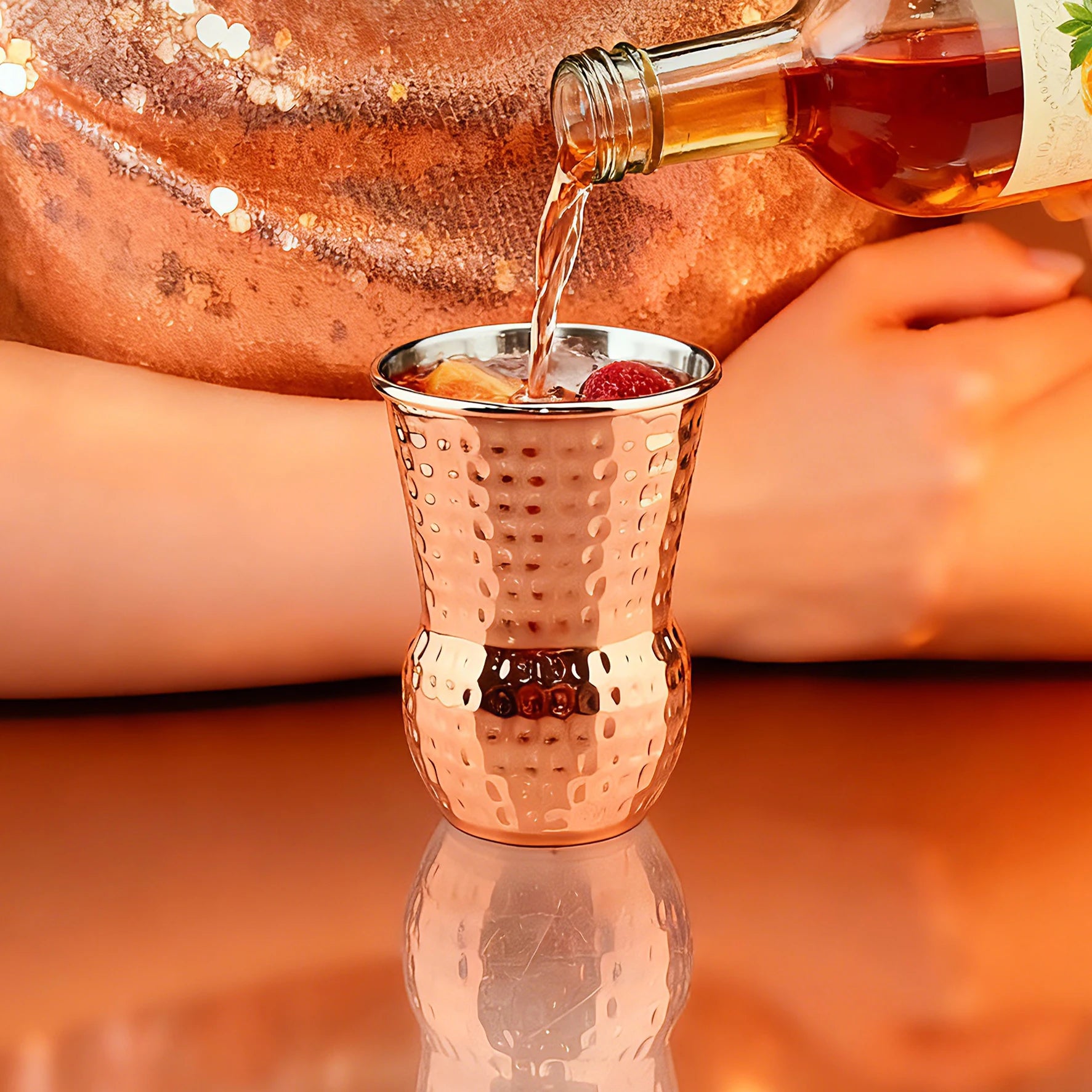 Gobelet tiki en inox cuivré, 350ml Nesty, cocktail ambré versé depuis une bouteille, glaçons, fraise et agrume dans le gobelet