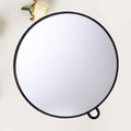 Miroir rond suspendu Nesty - Cadre noir sur fond crème avec une fleur en reflet, anneau d'accroche visible