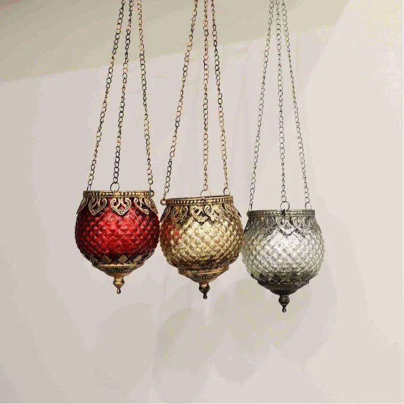 Trio de photophores suspendus en verre Nesty - Trois photophores facettés rouge, doré et argenté suspendus par des chaînes, sur fond blanc