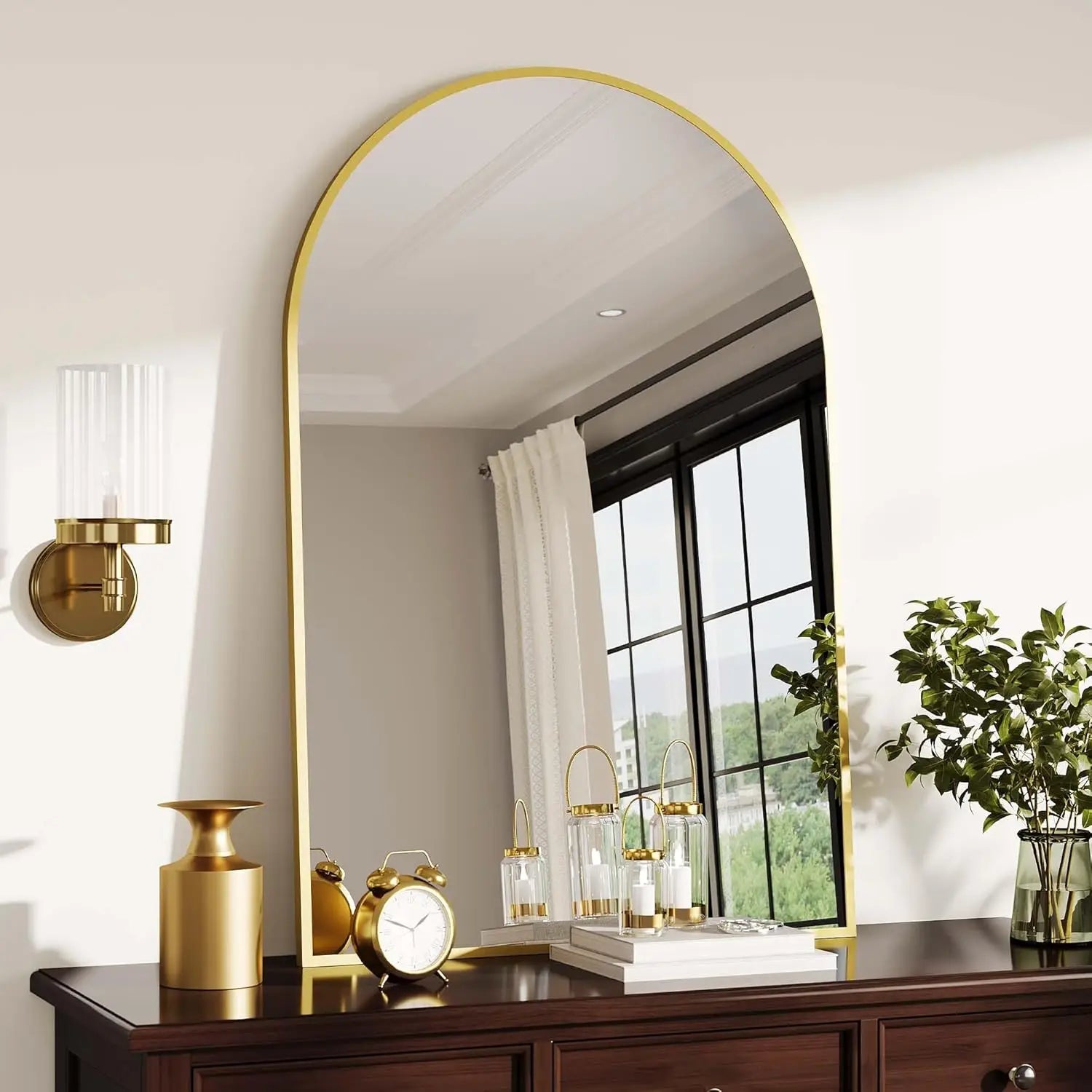 Miroir cintré cadre métal Nesty - Noir ou doré, variante cadre doré posée sur une commode en bois foncé avec réveil, lanternes à bougies et plante