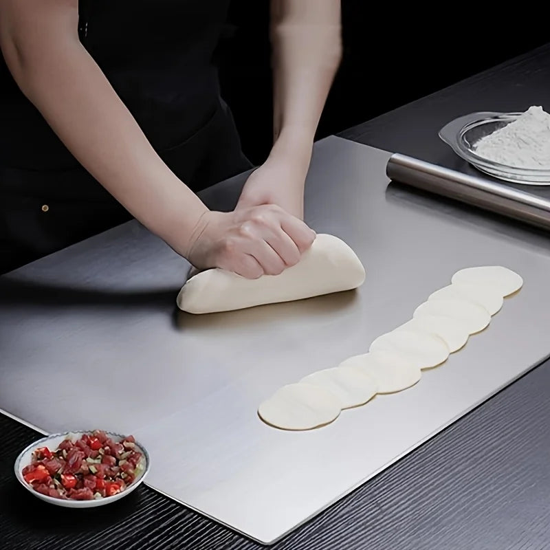 Planche à découper en acier inoxydable, antidérapante Nesty, mains pétrissant de la pâte et découpant des cercles de pâte à raviolis sur la planche en acier, bol de garniture à côté