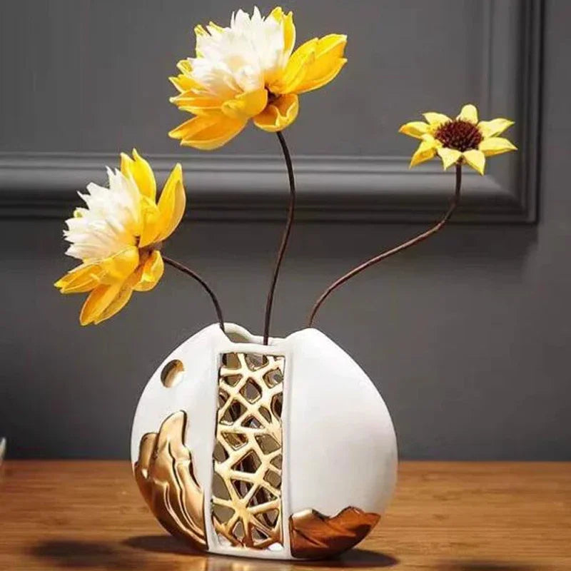 Vase en céramique blanche Nesty - Forme galet à découpe dorée ajourée, avec fleurs jaunes et blanches, sur table en bois