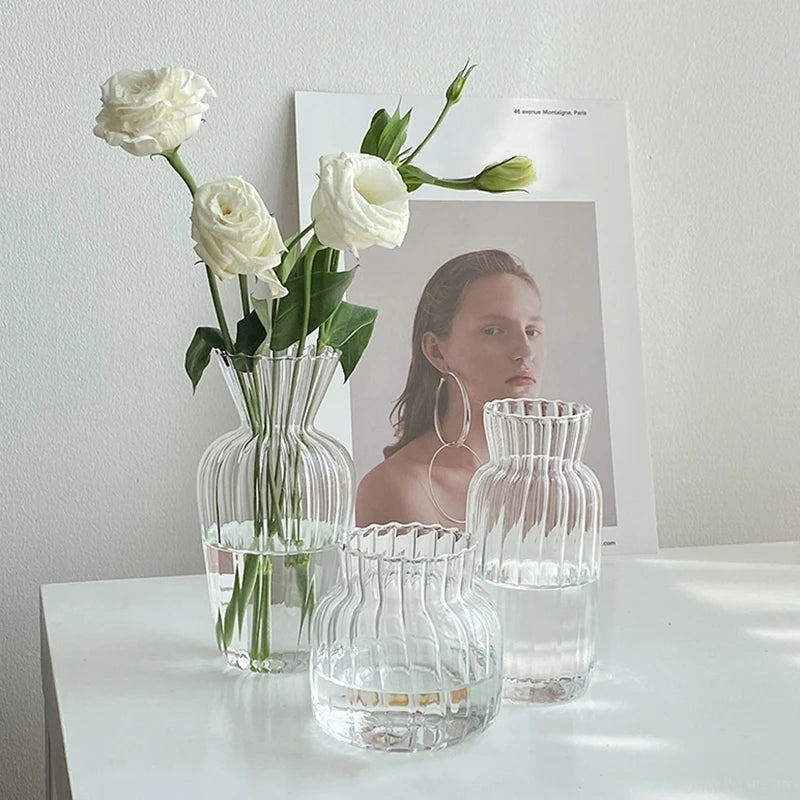Vase en verre transparent strié, mini format rétro Nesty, trois formes côtelées transparentes dont une garnie de roses blanches, sur bureau blanc