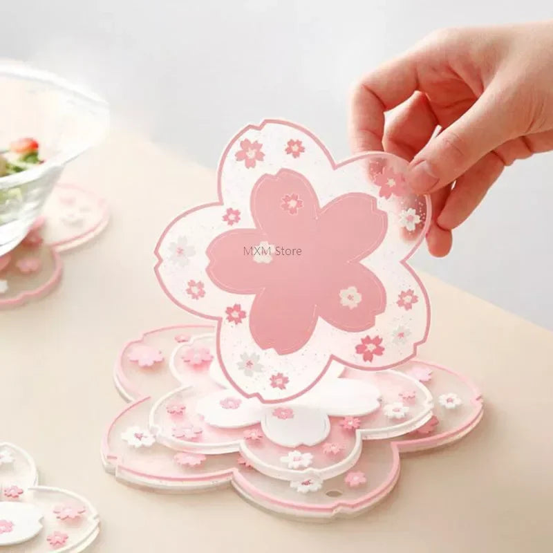Dessous de verre en silicone fleurs de cerisier rose, main tenant un exemplaire, empilés sur une table - Nesty