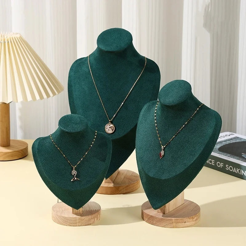 Buste en bois Nesty - Trois présentoirs en velours vert de tailles différentes avec colliers, près d'une lampe et de livres